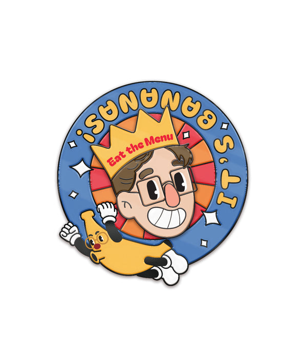 A spinning enamel pin made of two parts. The first part is Keith's face in the center adorning an "Eat the Menu" crown. The second part is a wheel with a Banana Zach and the phrase "It's Bananas!" that spins around Keith's face. From the Try Guys.